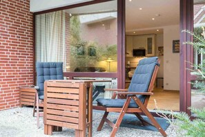 A modern outdoor seating area with wooden furniture and a glass door leading to a kitchen. - Apartment 2 rear (ID 014) - House Sandpeter (Sankt Peter-Ording)