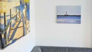 A room with a large painting of a beach scene on the left and a smaller painting of a lighthouse on the right.