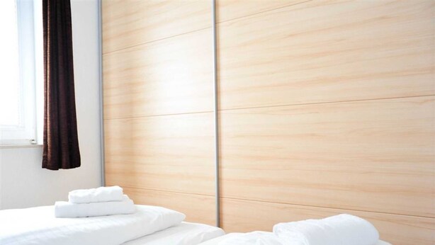 A hotel room with a wooden headboard, a window with curtains, and neatly folded white towels on the bed.