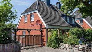 A traditional brick house with a sloped roof, a wooden gate, and a stone wall. - House section 8 Greetje (ID 261) (Sankt Peter-Ording)