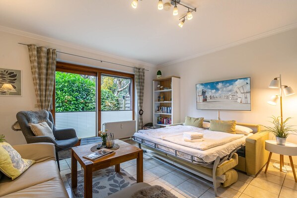 Une chambre moderne comprenant un lit, un canapé, une chaise, une petite table, une bibliothèque et une fenêtre avec des rideaux.