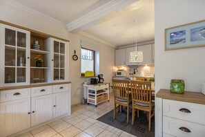 Une cuisine avec des meubles blancs, un coin repas avec des chaises en bois et un plan de travail blanc agrémenté d’un vase vert.