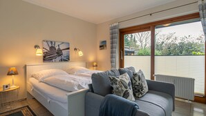 Une chambre à coucher avec un lit, un canapé gris, une table de chevet et une fenêtre avec des rideaux.