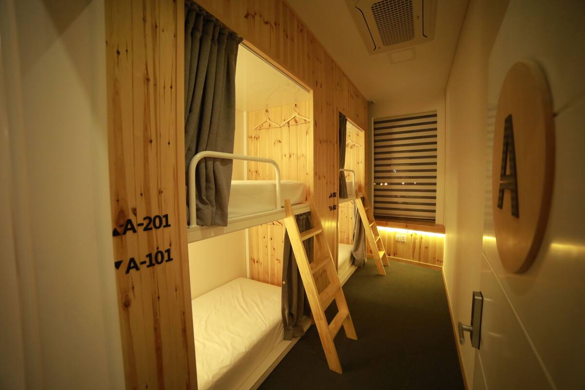 A cabin with bunk beds, wooden walls, and a small window with blinds.