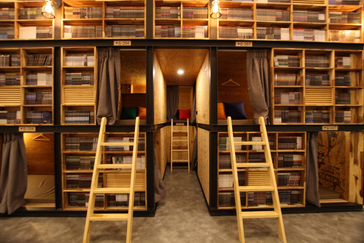 A library with bookshelves on both sides of a central walkway, wooden ladders, and a carpeted floor.