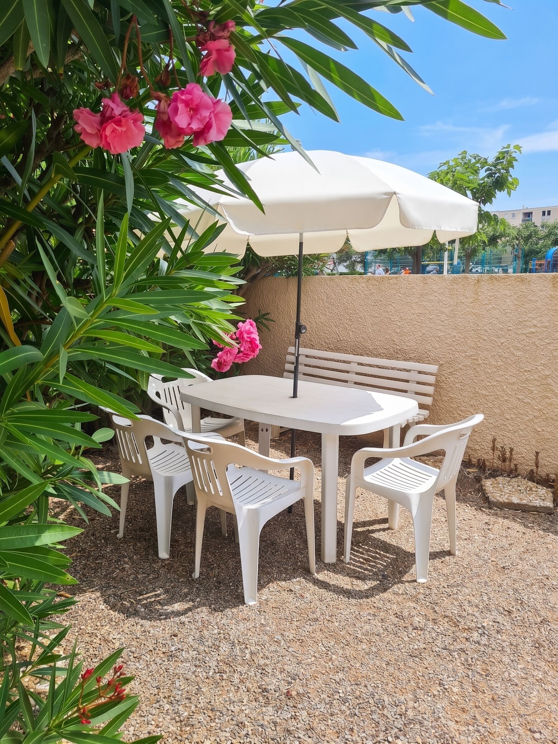 Un patio con una mesa y sillas blancas, un banco beige y una sombrilla blanca.