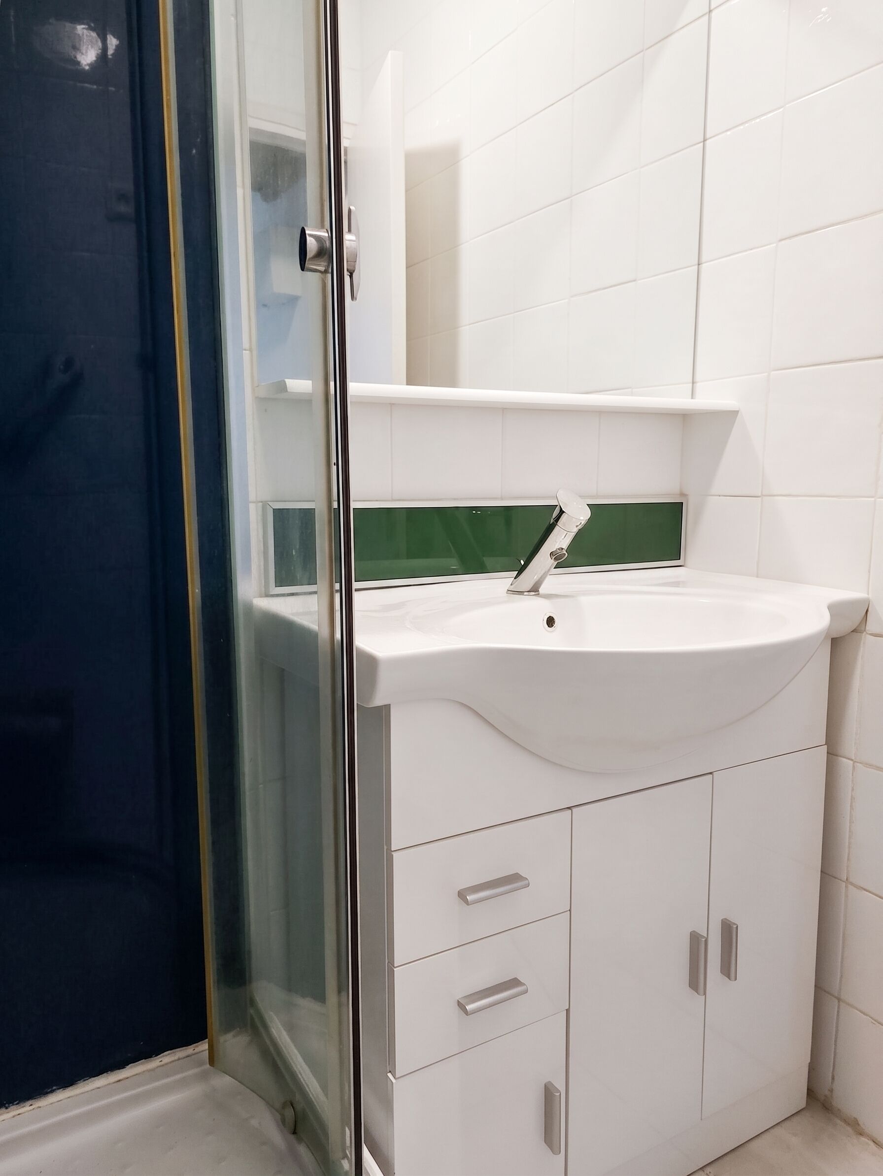 A bathroom with a white sink, a glass shower enclosure, and a white cabinet with drawers.