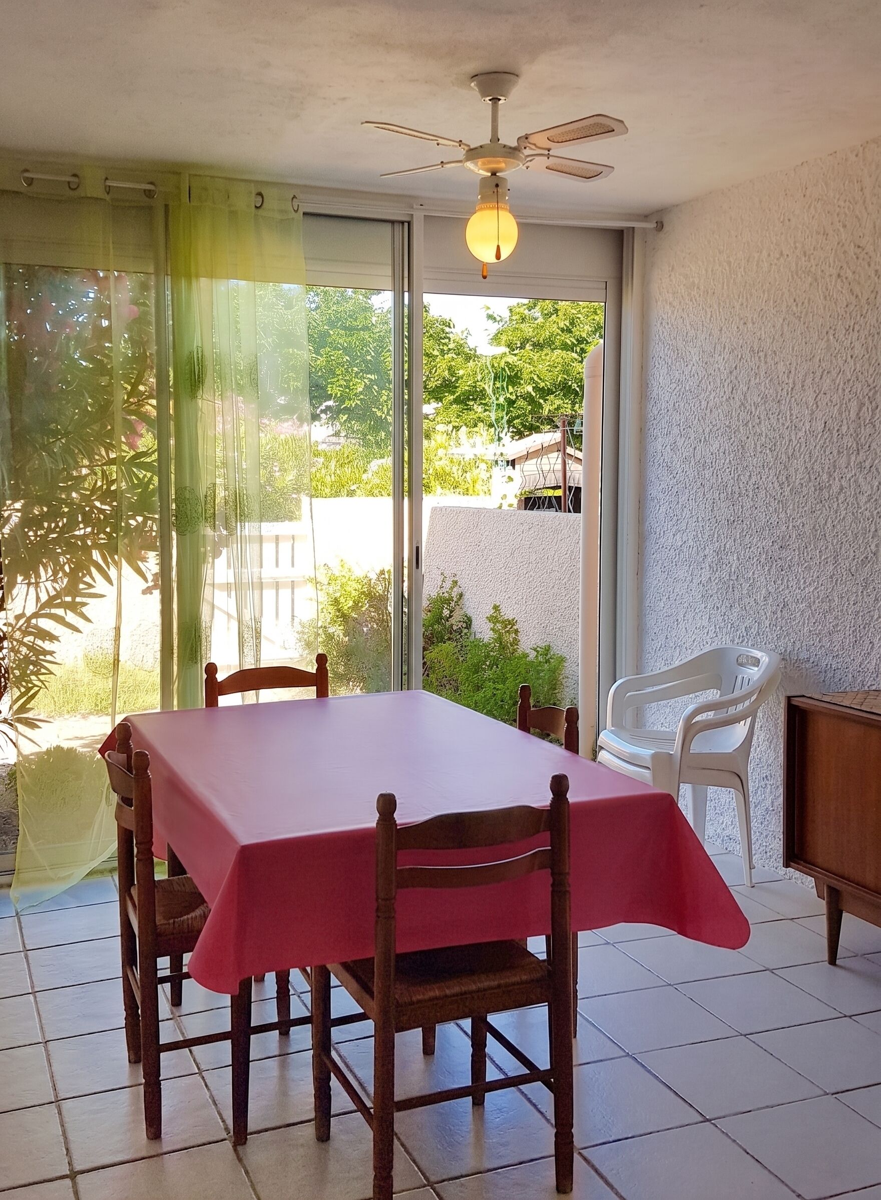 A dining area with a table and chairs, a ceiling fan, and a view through a glass door.