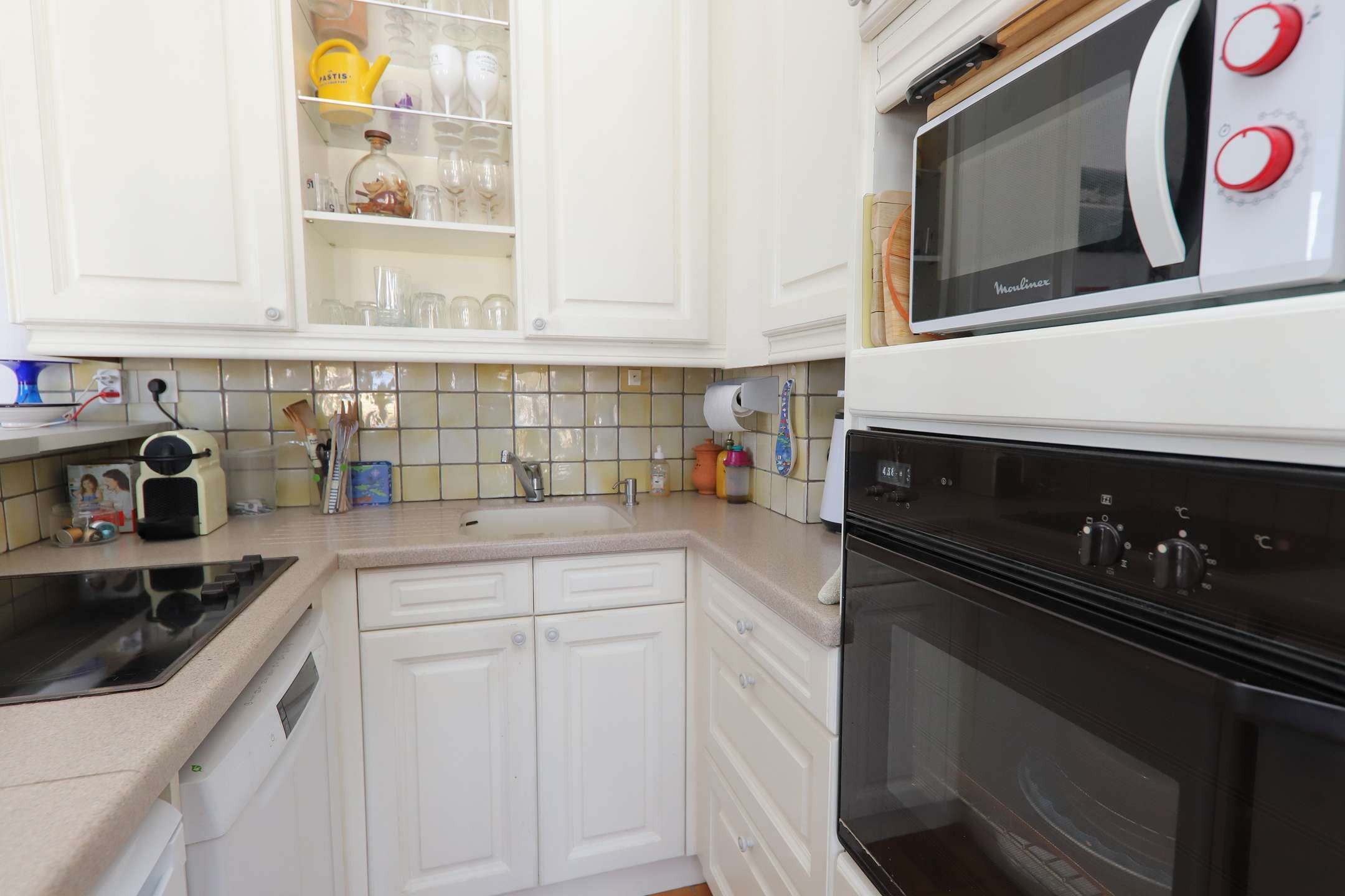 Una cocina con gabinetes blancos, microondas, horno y pileta.