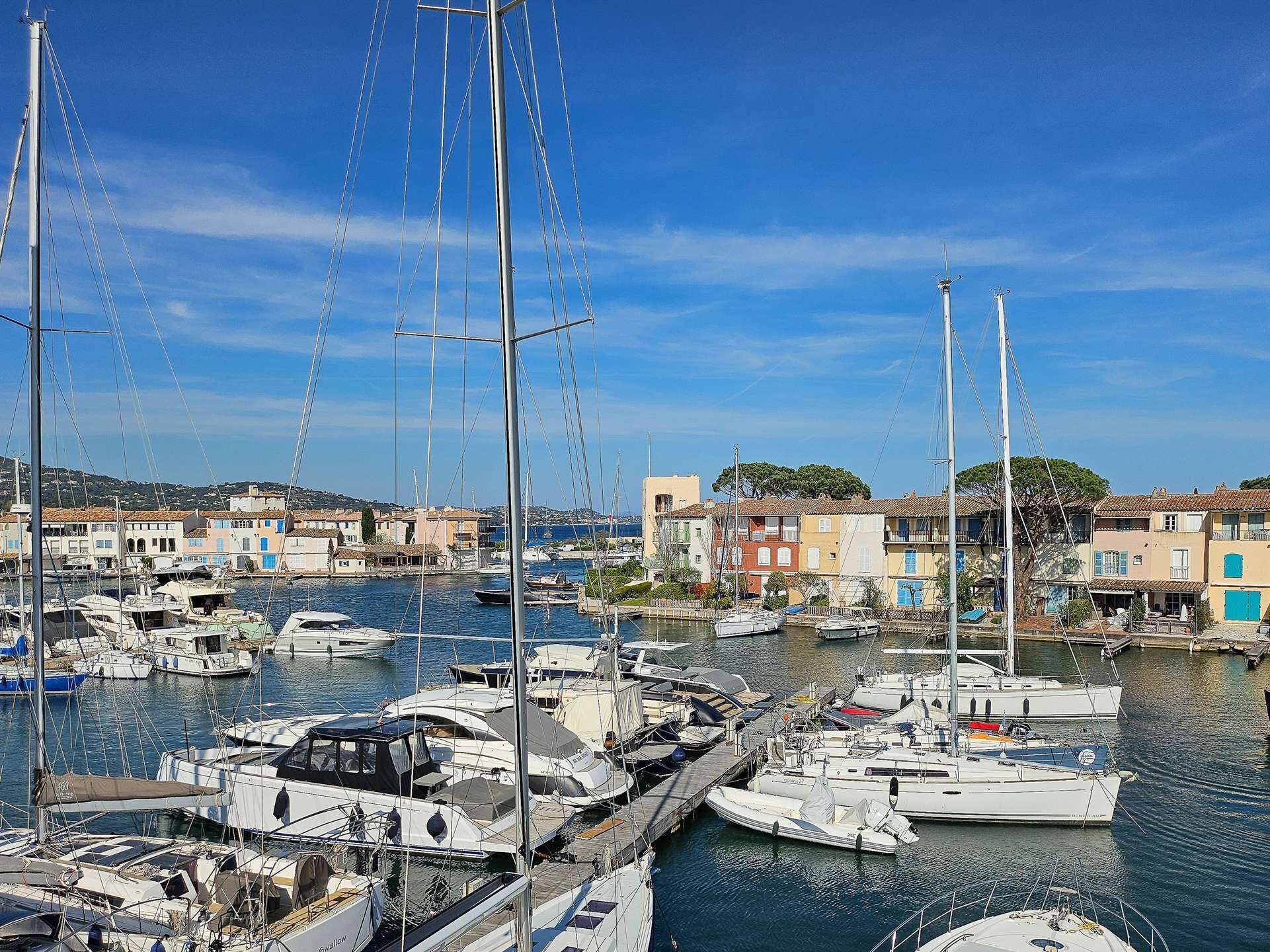 A marina with multiple boats docked, surrounded by buildings with Mediterranean architecture.