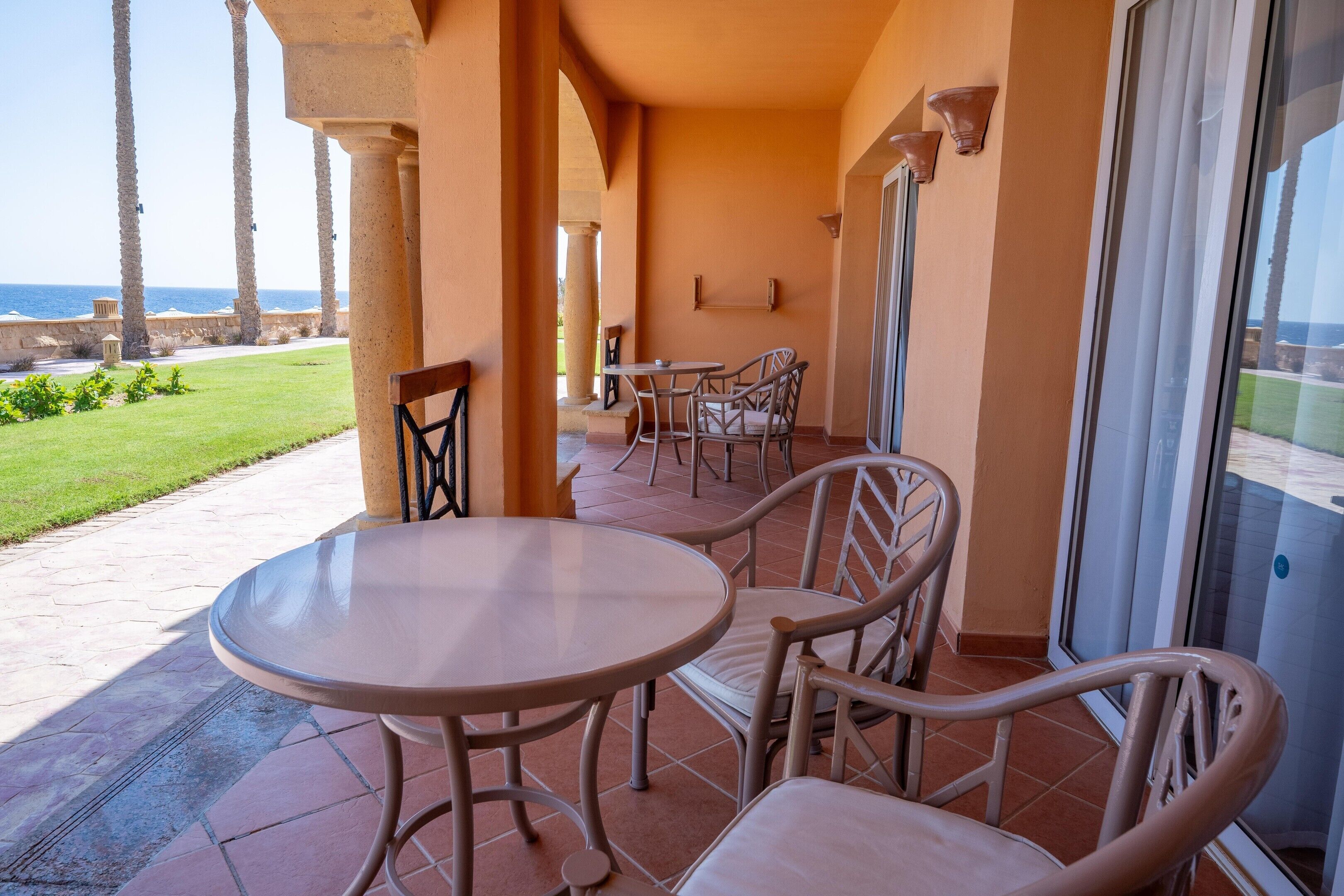 A terrace with a table and chairs, overlooking a grassy area and the sea.