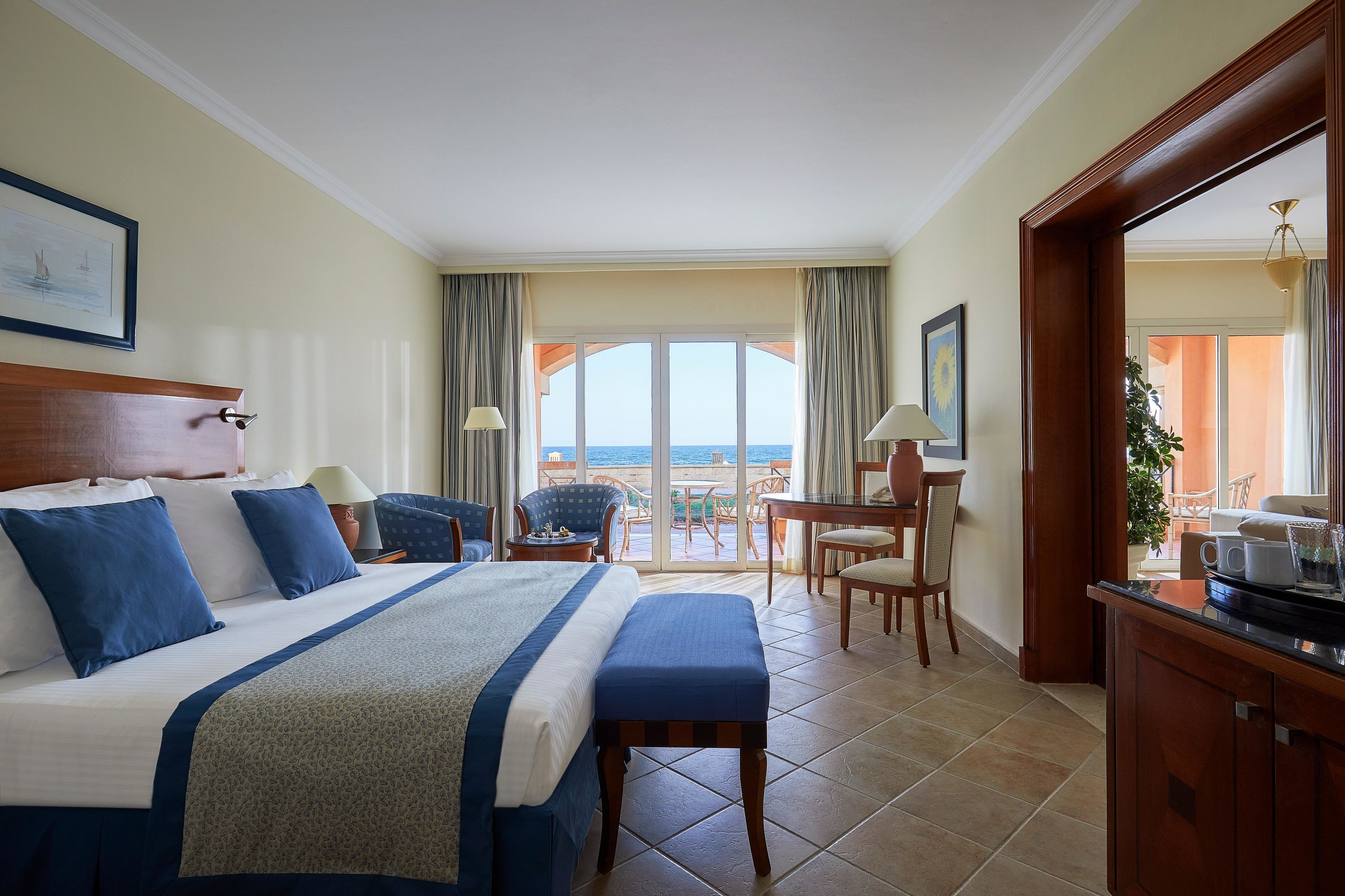 Une chambre d’hôtel avec un grand lit, un bureau, une chaise et une vue sur la mer.