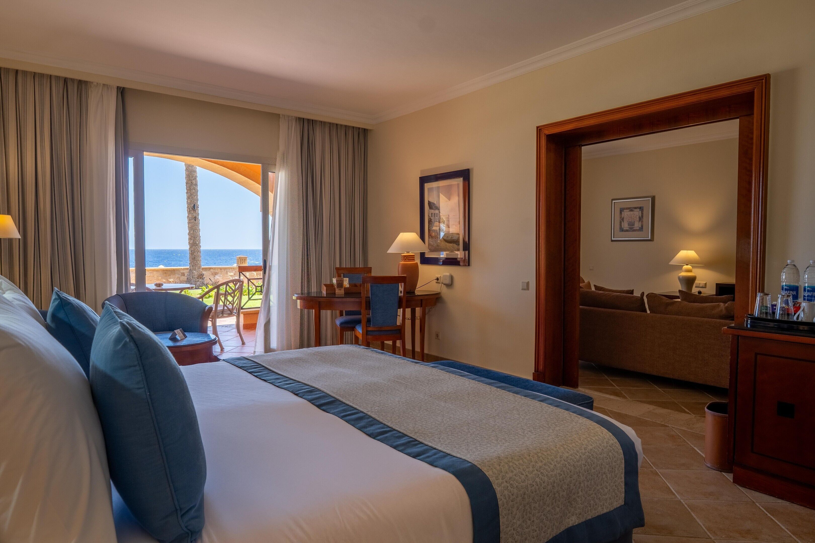 Ein Hotelzimmer mit einem großen Bett, einem Schreibtisch mit Stuhl, Meerblick und einem Balkon.