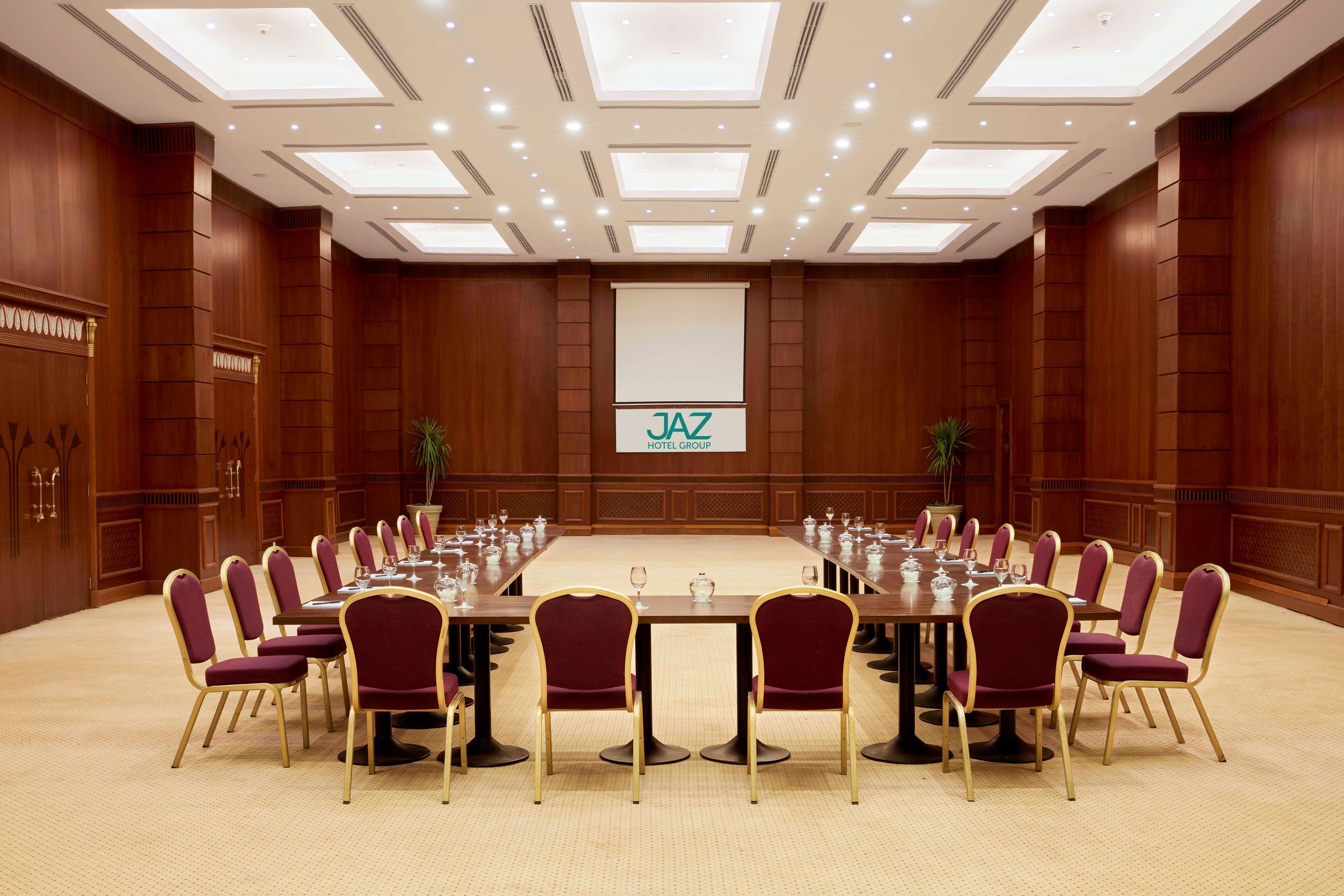 A conference room with a long table, chairs, and a screen displaying 'JAZ HOTEL GROUP'.