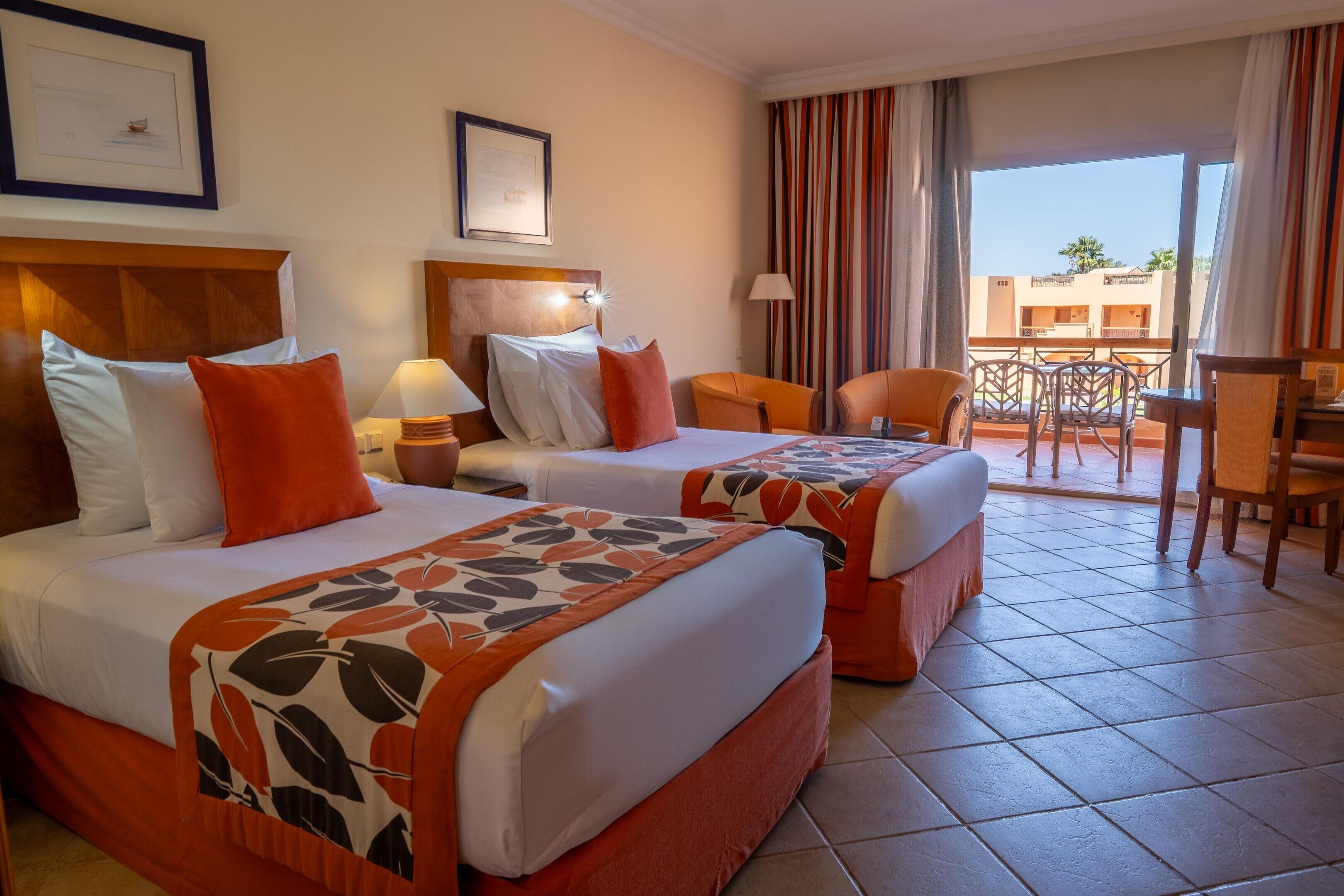 A hotel room with two beds, a desk, a chair, and a balcony with a view.