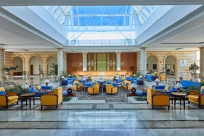A hotel lobby with a central seating area, a glass ceiling, and a reception desk. - JAZ Grand Marsa - All inclusive (El Quseir)