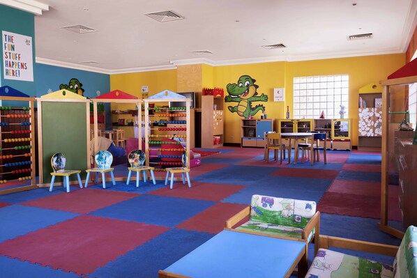 Un salón infantil con alfombras de colores, mesas de juegos y juguetes educativos.
