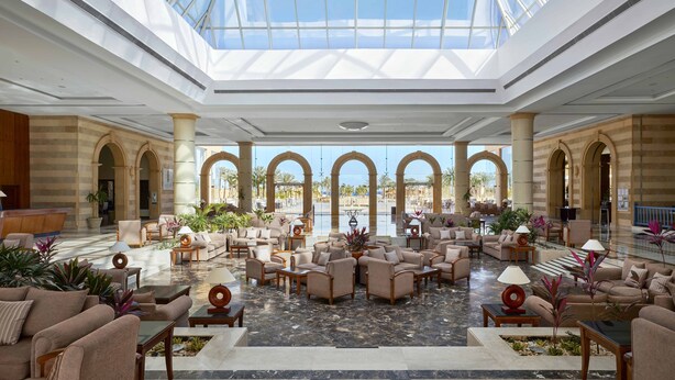 En rummelig lobby med højt til loftet og en glaskuppel, med behagelige siddeområder, en reception og udsigt ud.