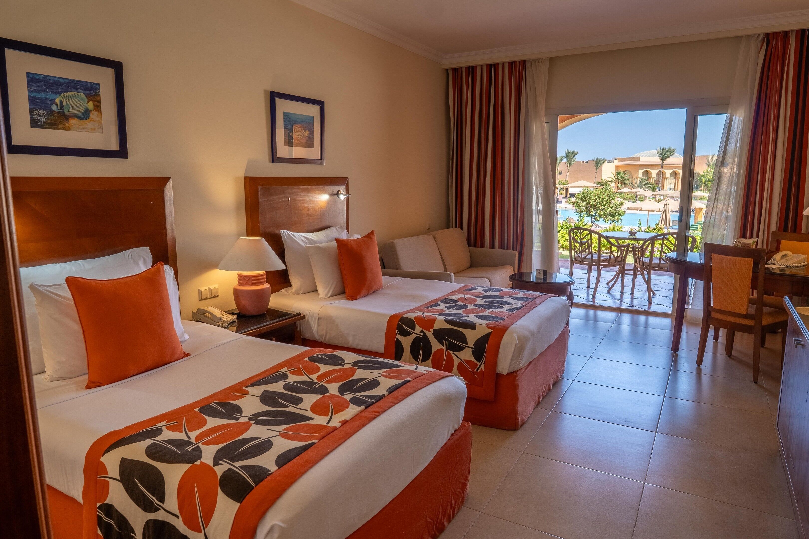 A hotel room with two beds, a sitting area, a balcony with a pool view, and a dining area.