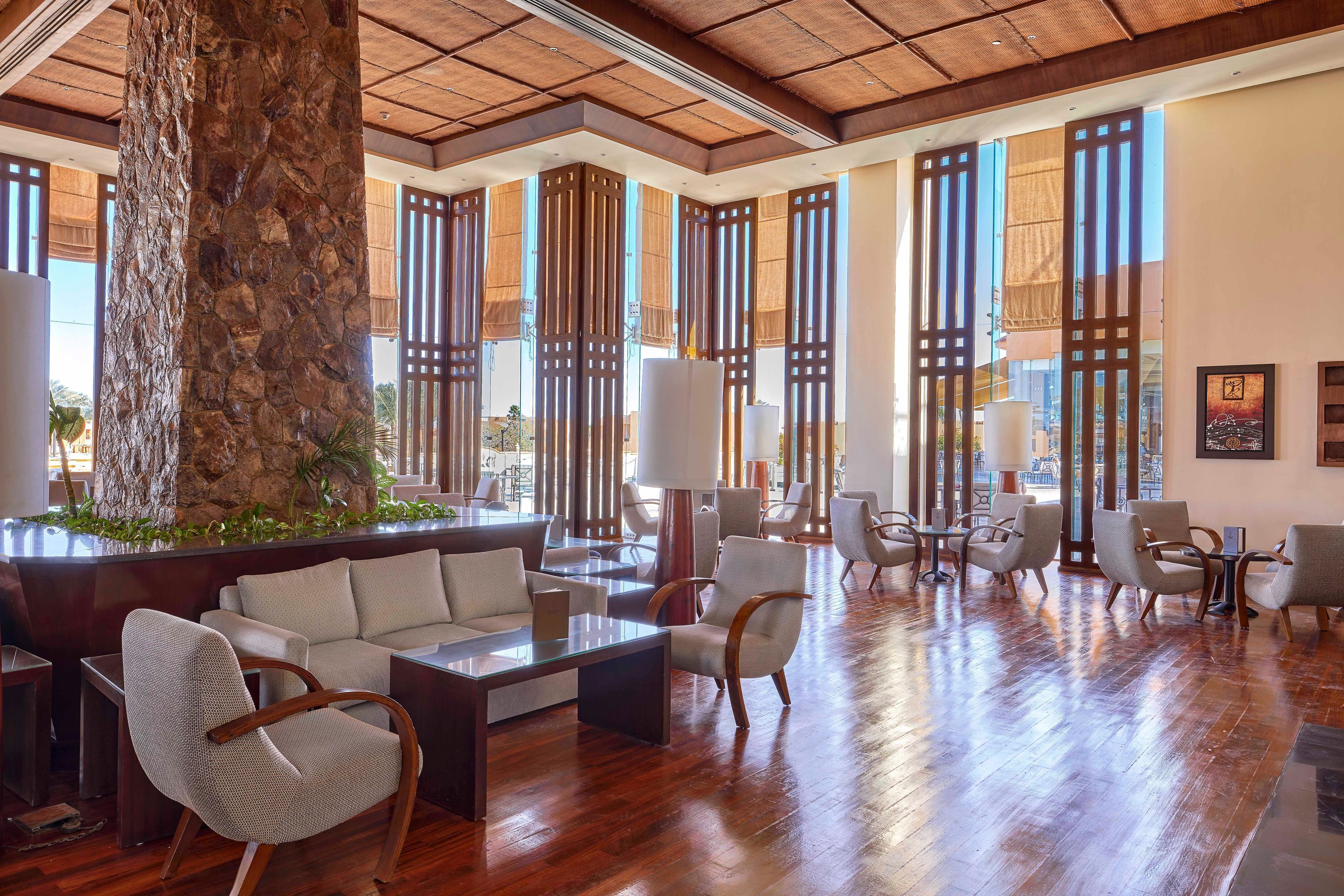 A spacious lobby with a large stone pillar, wooden flooring, and a seating area with sofas and armchairs.