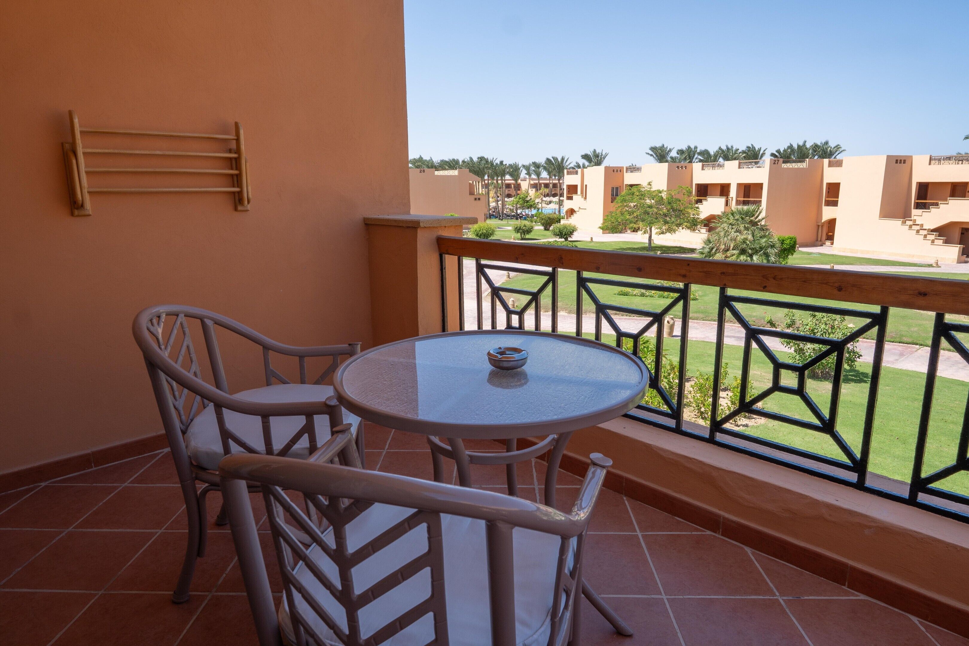 Un balcon avec une table ronde et deux chaises, une rambarde en métal et une vue sur un ensemble d’immeubles comportant plusieurs étages et balcons.