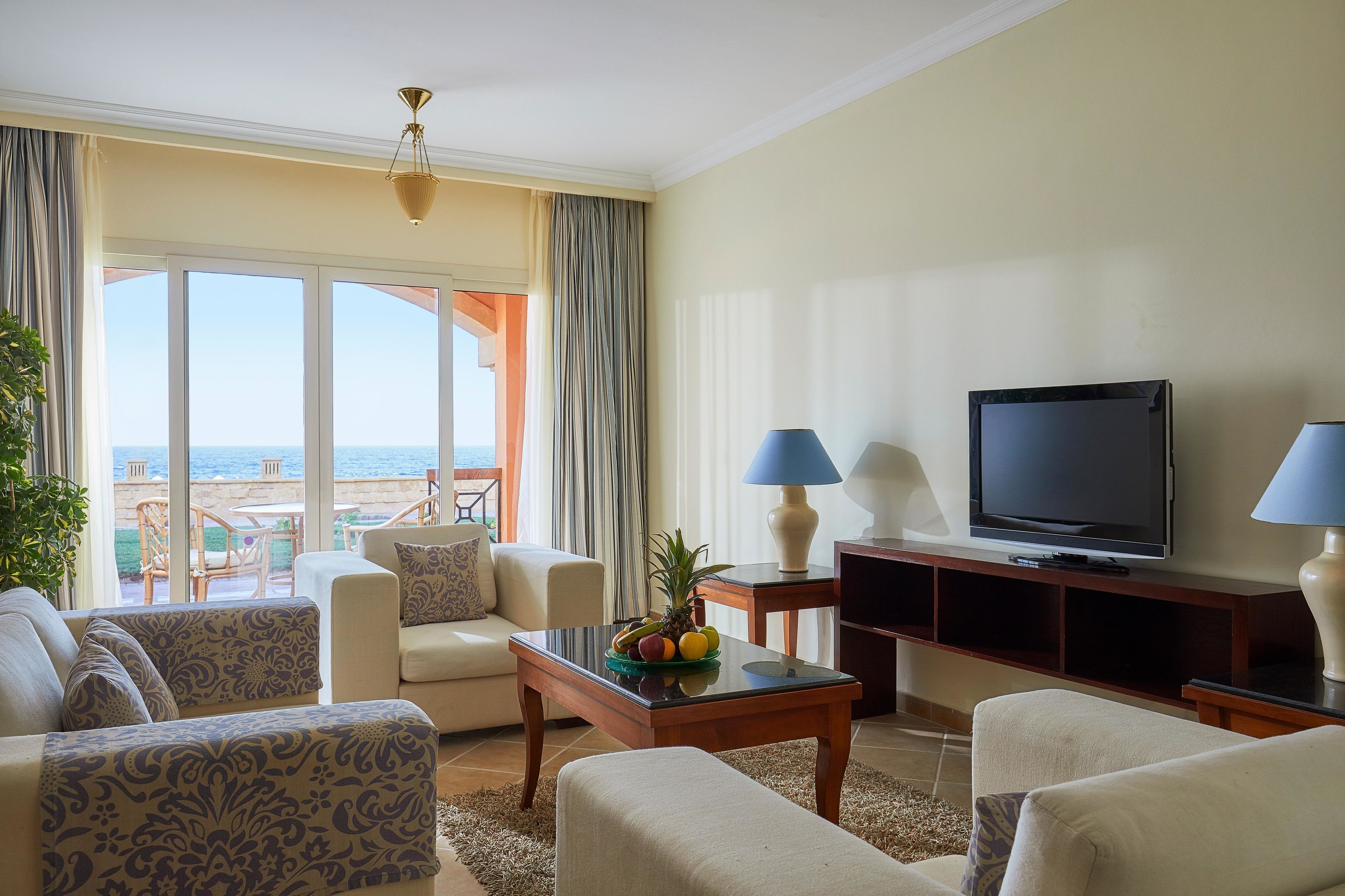 A hotel room with a balcony, a television, and a fruit bowl on the coffee table.