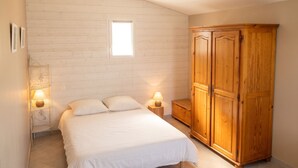 A bedroom with a bed, two bedside lamps, a wooden wardrobe, and a window. - Homerez - House in Sauzon (Sauzon)