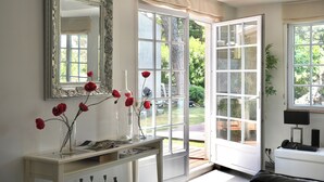 A room with a large mirror, a console table with vases, and a view of a garden through a glass door. - Villa Paradisiaque - La HUPPE de SAINT TROPEZ (Saint-Tropez)