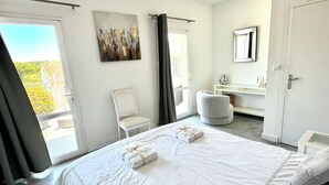 A bedroom with a large bed, a chair, a desk, and a bathroom area. - Villa Paradisiaque - La HUPPE de SAINT TROPEZ (Saint-Tropez)