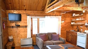 A cozy cabin interior with a sofa, a dining table, a kitchen area with a stove, and a mounted TV.