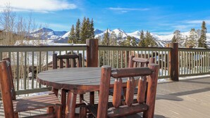 A wooden deck with a table and chairs, overlooking a snowy mountain range. - Spacious. Private Hot Tub.Views. Deck. Pool Table. (Breckenridge)