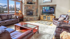 A cozy living room with leather sofas, a stone fireplace, a television, and a view of snow-capped mountains. - Spacious. Private Hot Tub.Views. Deck. Pool Table. (Breckenridge)