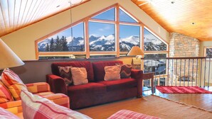 A cozy living room with a large window offering a mountain view, a red sofa, and a wooden ceiling. - Spacious. Private Hot Tub.Views. Deck. Pool Table. (Breckenridge)