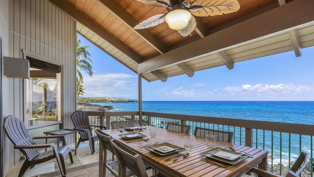A wooden deck with a table set for dining, overlooking a beach and ocean.