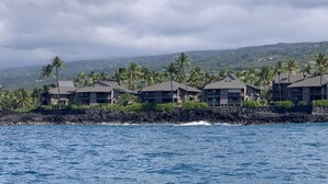 A coastal hotel with multiple buildings, a rocky shoreline, and palm trees.