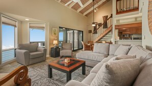A spacious living room with a high ceiling, a large sofa, a coffee table, and a staircase leading to an upper level.