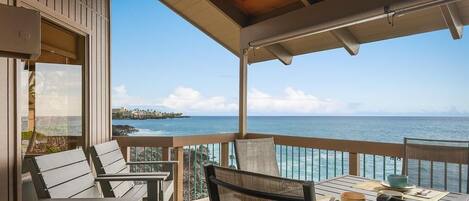 A covered outdoor seating area with a table and chairs, overlooking a clear blue sea and a distant shoreline.