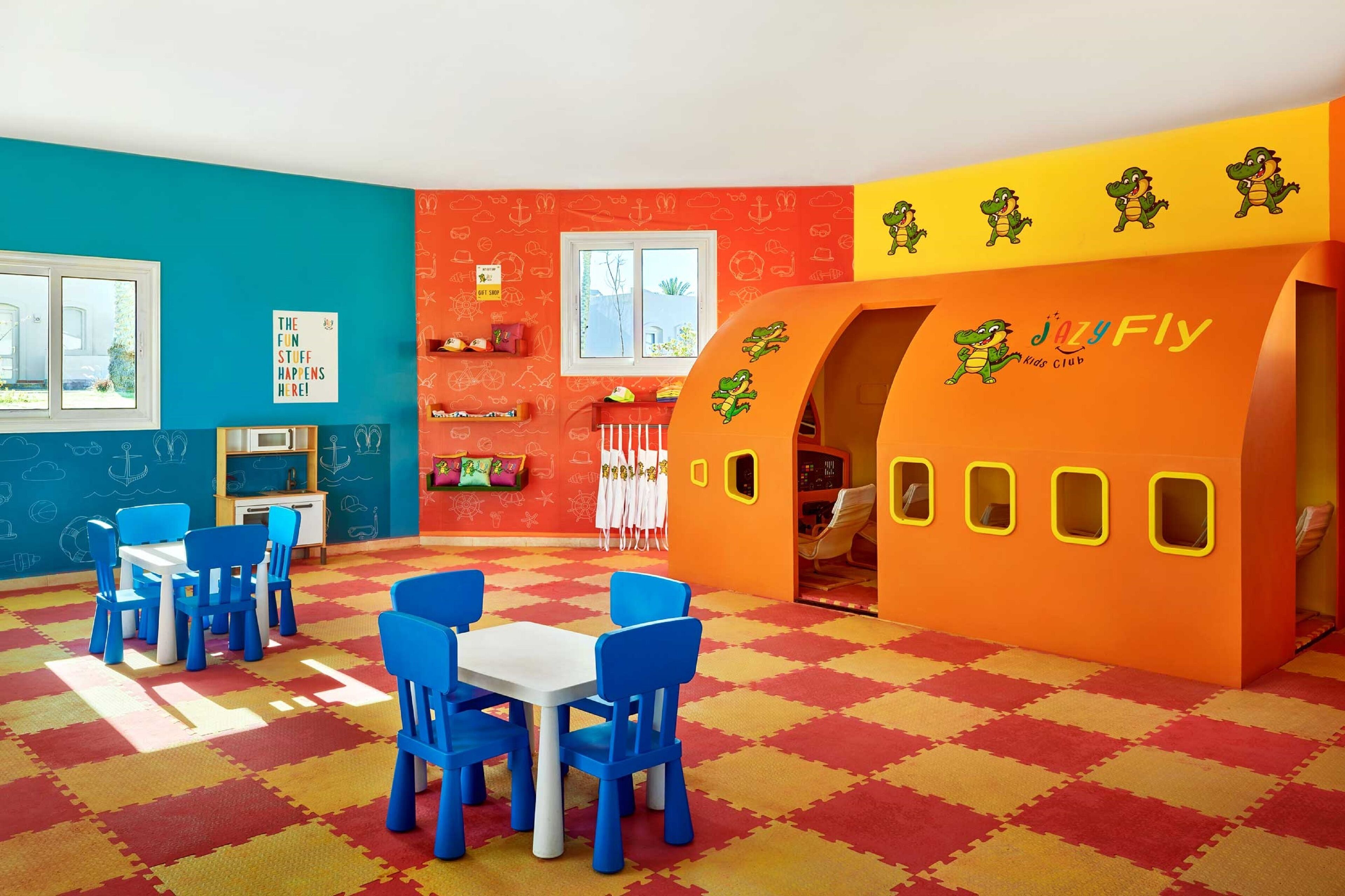 A children's playroom with a colorful interior, including a playhouse, blue chairs, and a red and yellow checkered floor.