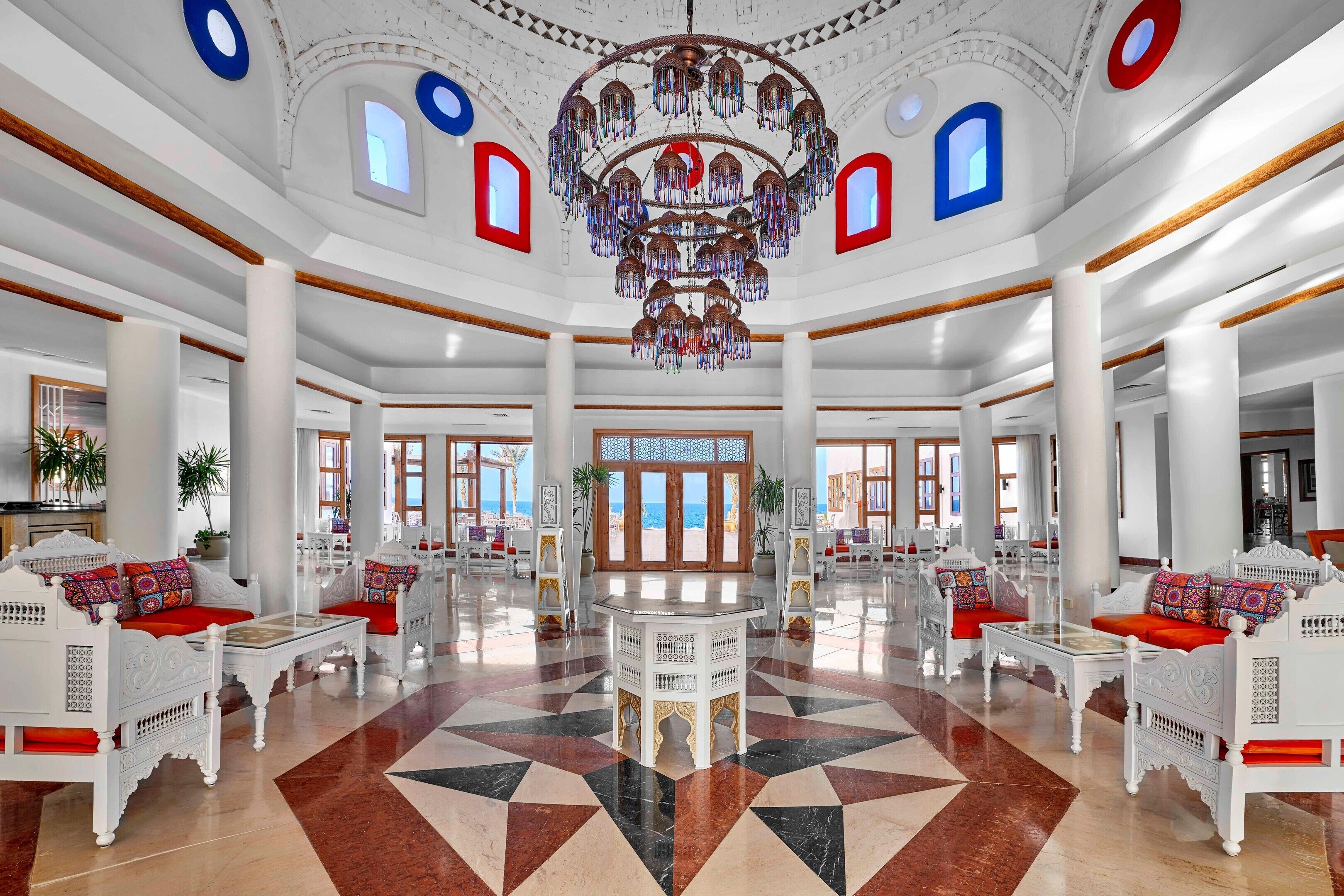 A spacious lobby with a geometric patterned floor, white ornate furniture, and a large chandelier.