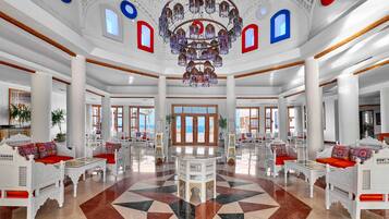 A spacious lobby with a geometric patterned floor, white ornate furniture, and a large chandelier.