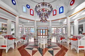 A spacious lobby with a geometric patterned floor, white ornate furniture, and a large chandelier.