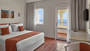 A hotel room with a bed, a desk, a TV, a painting, and a view of the sea.
