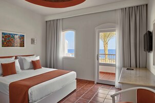 Habitación de hotel con cama, escritorio, televisor, un cuadro y vista al mar.