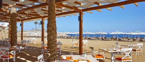 Un espace de restauration en plein air avec des tables et des chaises, une pergola et une vue sur la plage et l’océan.