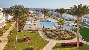 A resort with a swimming pool, palm trees, and a view of the sea.
