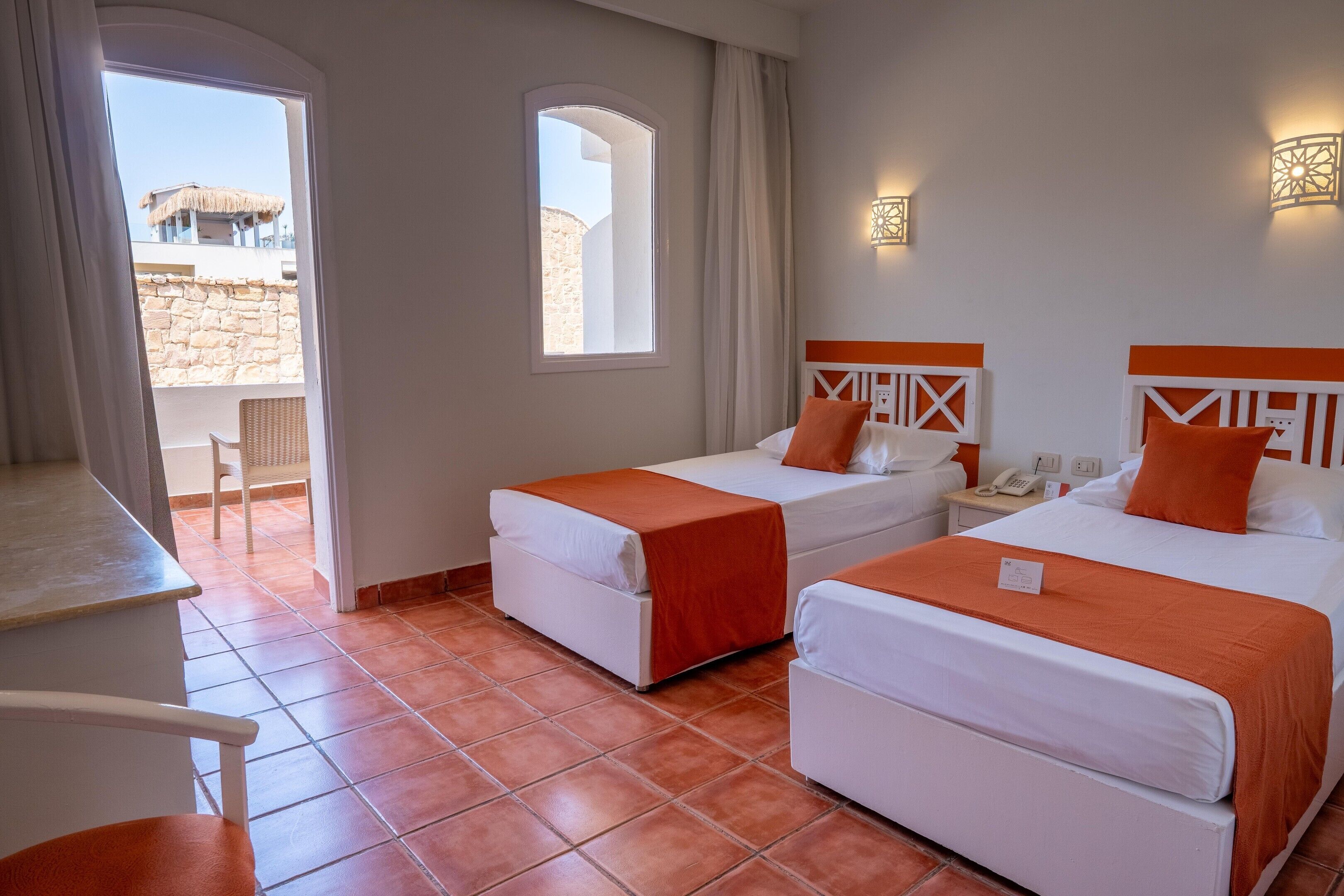 A hotel room with two beds, a desk, and a view of the outside.