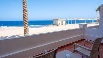 Un balcon avec des fauteuils en osier et une petite table, donnant sur une plage et offrant une vue dégagée sur l’océan.
