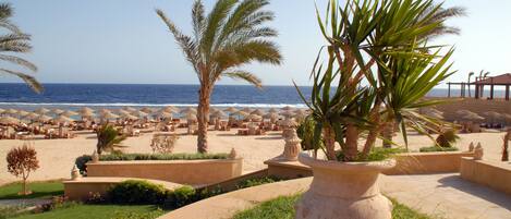 A beach resort with palm trees, sun loungers, and umbrellas.