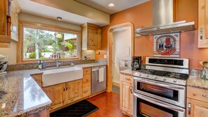 A modern kitchen with granite countertops, stainless steel appliances, wooden cabinets, and a large window providing natural light. - BEST YARD + HOUSE 🏡🤩Hot tub, fire pit, grill, gym, and soaking spa bathtub! (Colorado Springs)