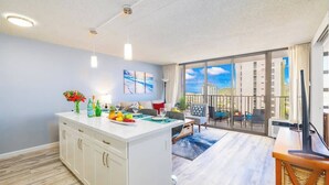 A modern kitchen with a central island, a dining area with a view, and a balcony with a cityscape view. - Ocean-view condo near Waikiki Beach (Honolulu)